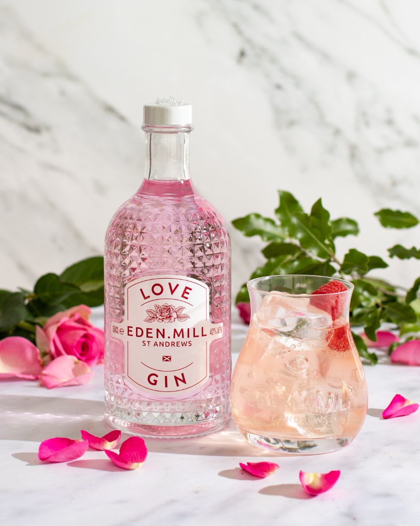 Pink Gin in a crystal effect bottle. A glass filled with ice and gin with a raspberries on top.